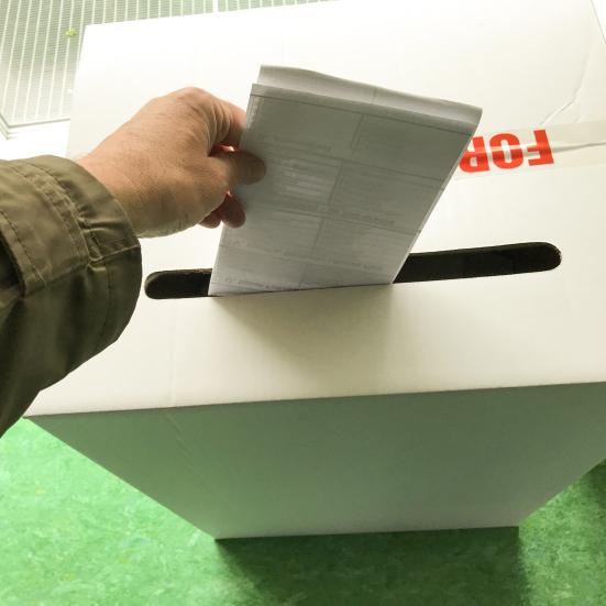 Hånd lægger valgseddel i stemmeurne