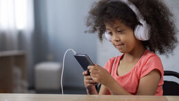 Barn med høretelefoner på ørerne og smartphone i hånden